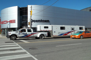 Ein Polizei-Lkw vor einem Gebäude mit Text geparkt, eine Ampel mit Stange und Drähten im Vordergrund und Bäume mit klarem blauem Himmel im Hintergrund.