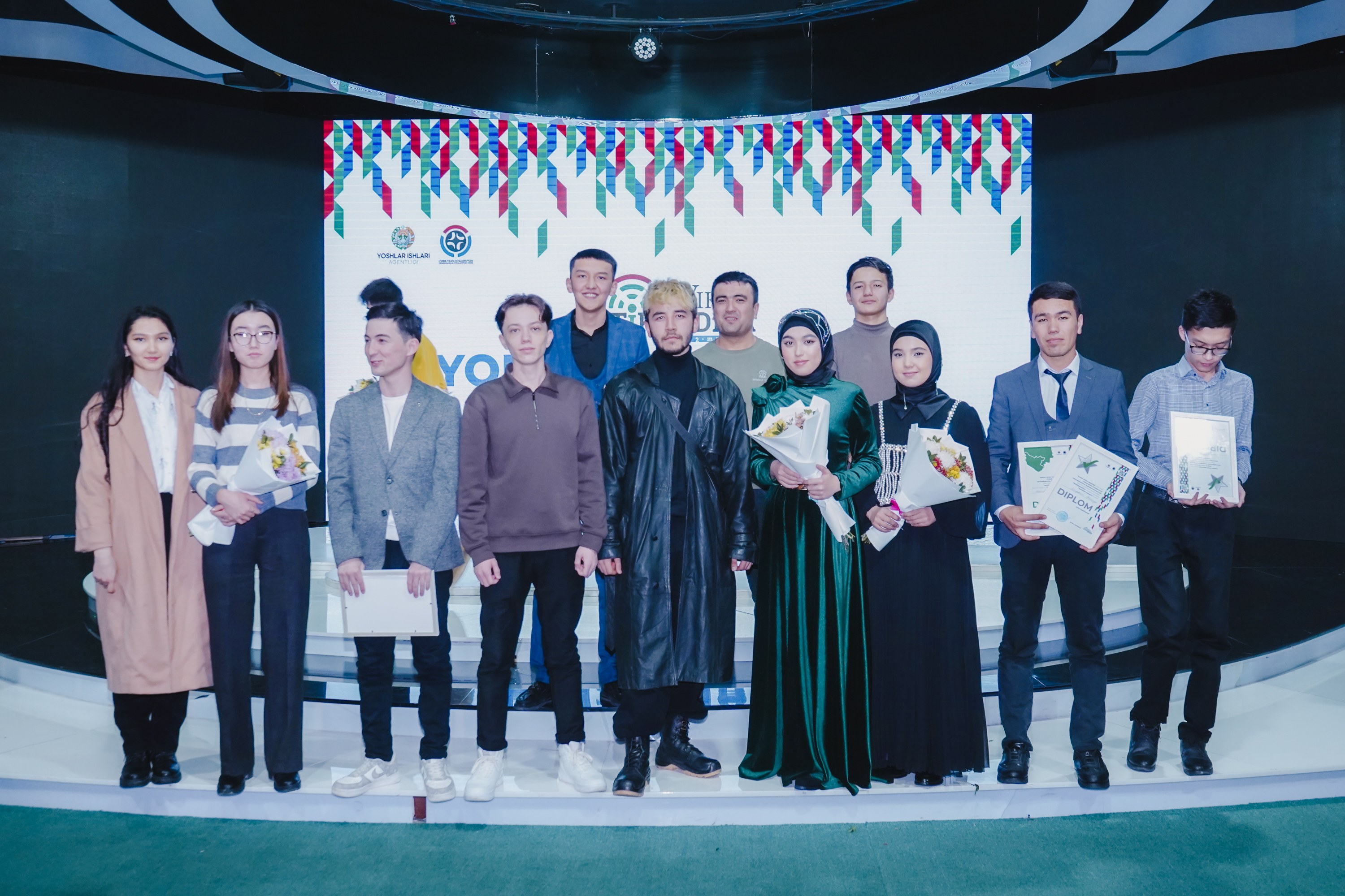 Gruppe von Menschen auf einer Bühne mit Blumenstr├Ąuessen und Urkunden, im Hintergrund ein 'Jugend-Solar-Awards 2019'-Plakat