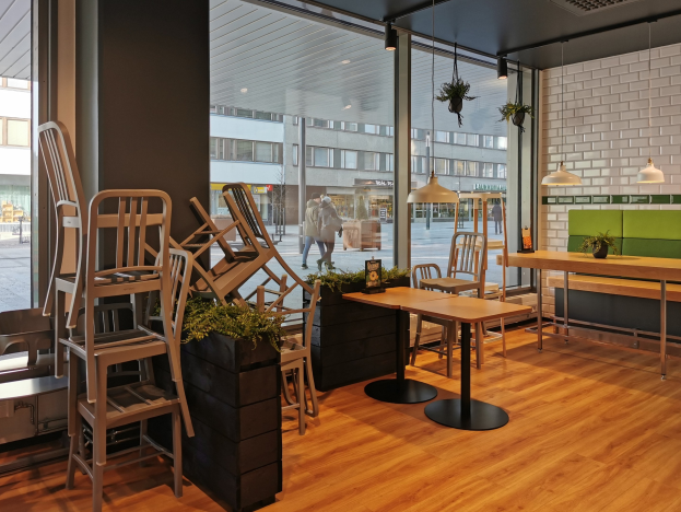 Ein Restaurant-Innenraum mit Holztischen und -stühlen in der Nähe eines großen Fensters, das eine Straßenansicht von Berlin mit Fußgängern, Gebäuden und urbanen Elementen zeigt.