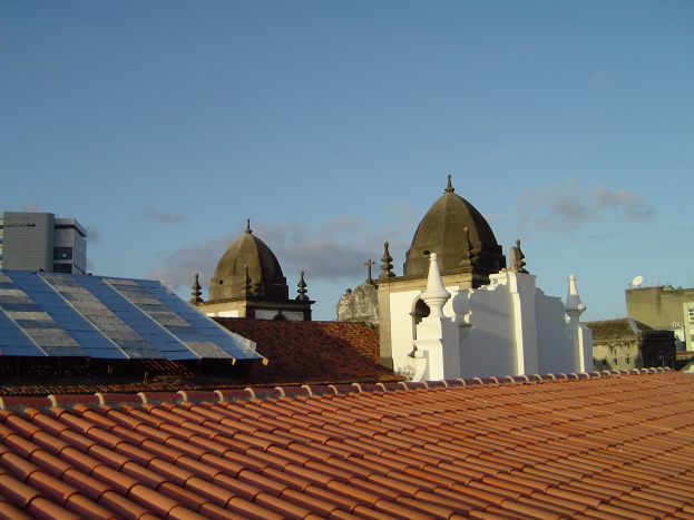 Stadtansicht mit mehreren Gebäuden im Vordergrund, einem klaren blauen Himmel im Hintergrund und Solarpanelen auf einem Dach.