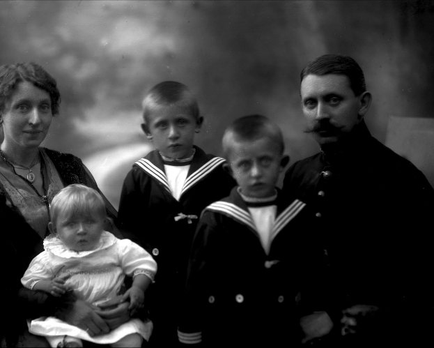 Schwarz-weiß-Foto einer Frau, die ein Baby hält, mit zwei Jungen daneben, Hintergrund leicht unscharf.