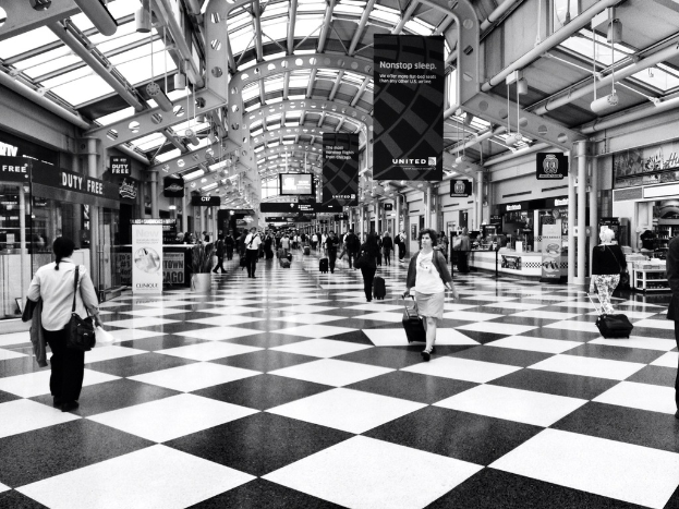 Menschen mit Taschen gehen in einem Geb├Ąude mit Gesch├Ąften und Schildern.