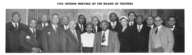 Eine Gruppe von Männern in Anzügen lächelt gemeinsam vor einer Wand, mit Text oben und unten, der "1955 Zwischenversammlung des Vorstands" lautet, in Schwarz-Weiß.