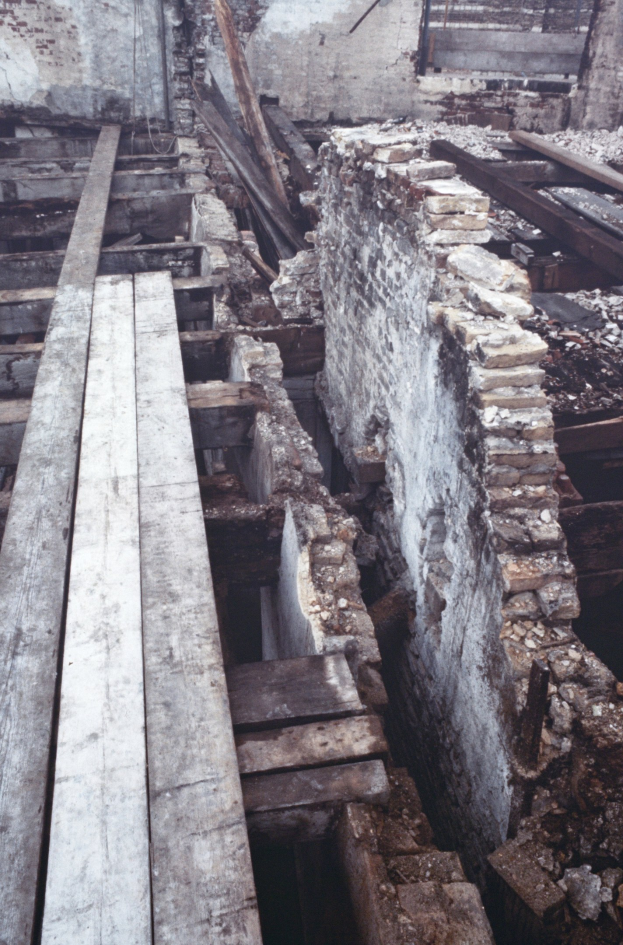 Altes Gebäude beim Abriss mit verstreuten Holzplanken, Steinen und einer sichtbaren Wand im Hintergrund.