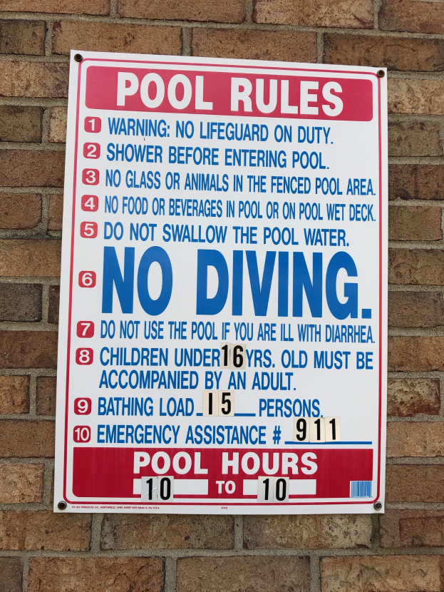 Weißes Schild mit schwarzer Schrift, das "Pool Rules: No Diving" an einer Backsteinmauer angebracht ist.
