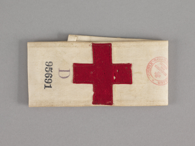 Ein rotes Kreuz-Ersthelfer-Set in einer Stofftasche mit Text und einem Stempel, auf einer Oberfläche platziert.