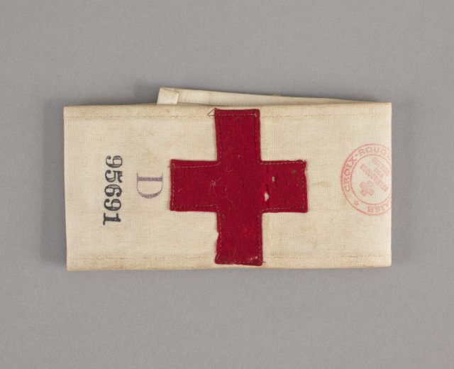 Ein rotes Kreuz-Ersthelfer-Set in einer Stofftasche mit Text und einem Stempel, auf einer Oberfläche platziert.