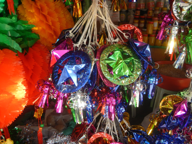 Eine festliche Deckeninstallation mit farbigen Papierlaternen, Bändern und Dekorationen, die über Regalen mit Flaschen im Hintergrund hängen.