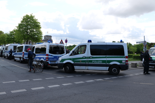 Eine Gruppe von Polizeiwagen, die an einer Straße geparkt sind, mit einem Radfahrer im Vordergrund und Gebäuden, Bäumen und Schildern im Hintergrund.