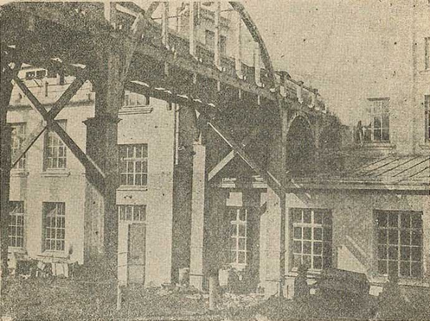 Schwarzes und weißes Foto eines im Bau befindlichen Gebäudes aus den 1890er Jahren, das Fenster, Säulen und einen Himmelhintergrund zeigt, mit dem Text '1890er Jahre - Bau einer Eisenbahnbrücke' unten.