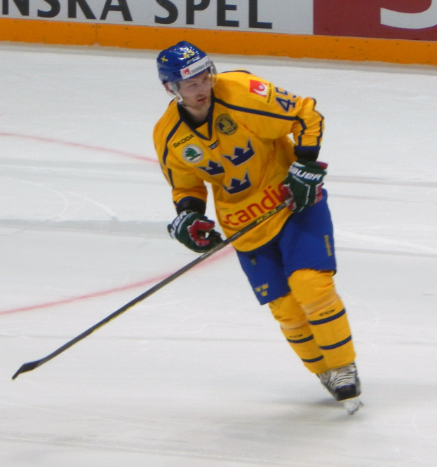 Eishockeyspieler in Bewegung auf dem Eis mit Schutzausrüstung und einem Stock in der Hand, mit einer textgefüllten Tafel im Hintergrund.